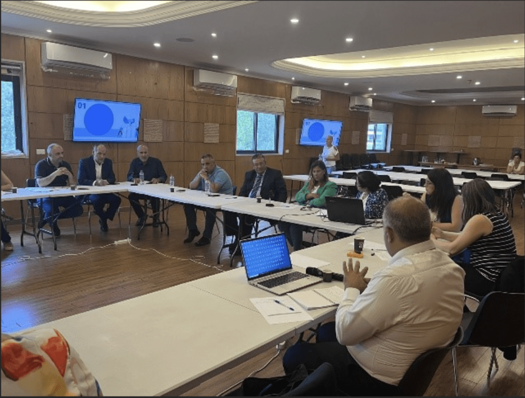 Group of individuals sitting at tables in a conference room, engaged in a meeting.
